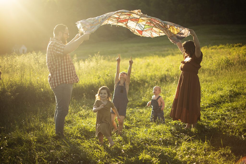 mom and dad are playing parachute with kids running under a quilt during baltimore family photo session