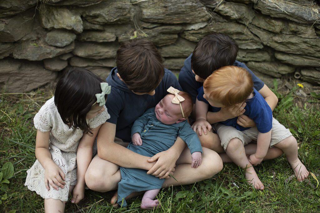 four older siblings looking at newborn sister during in home newborn session in baltimore