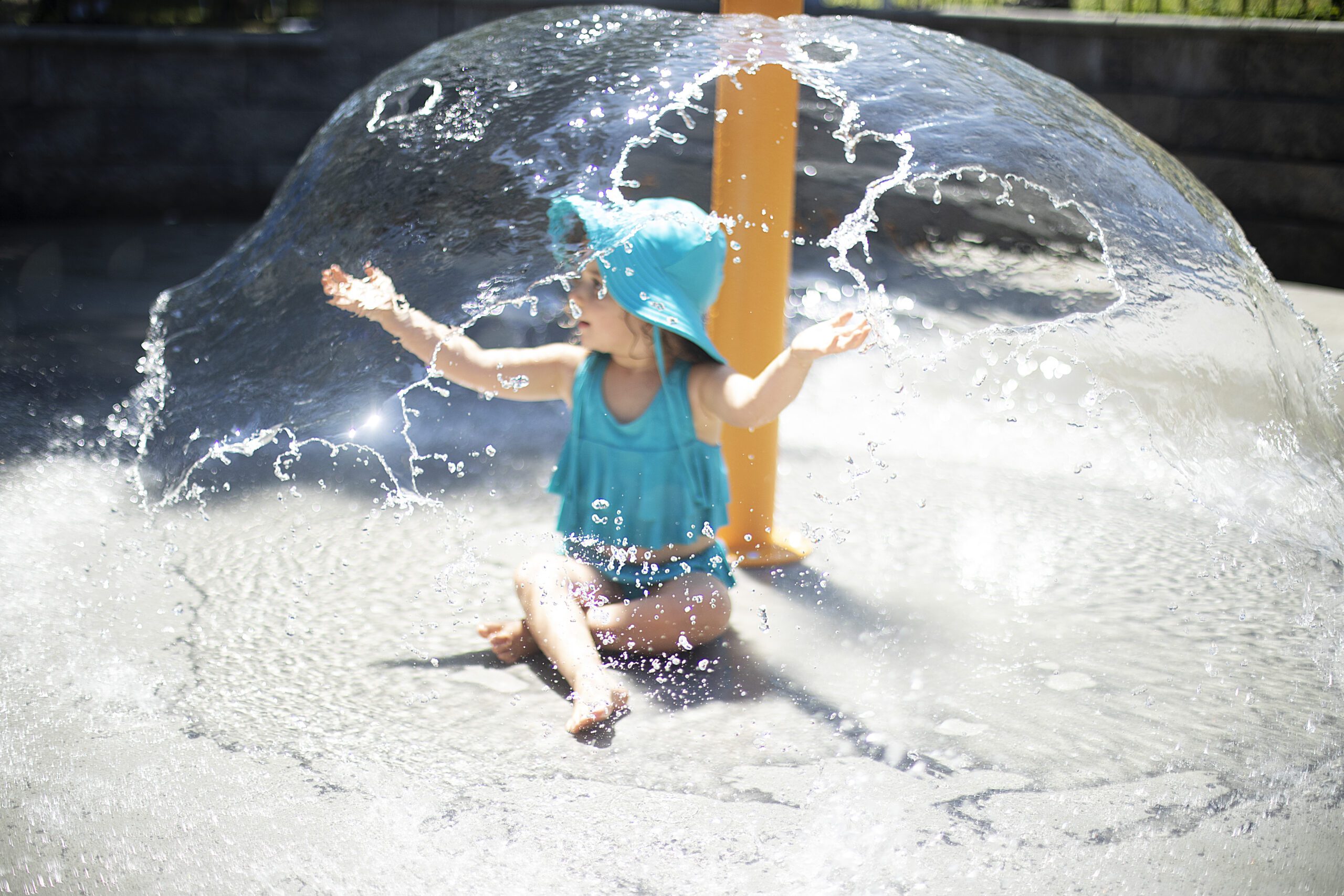 girl sitting under water fountain at baltimore splash pad