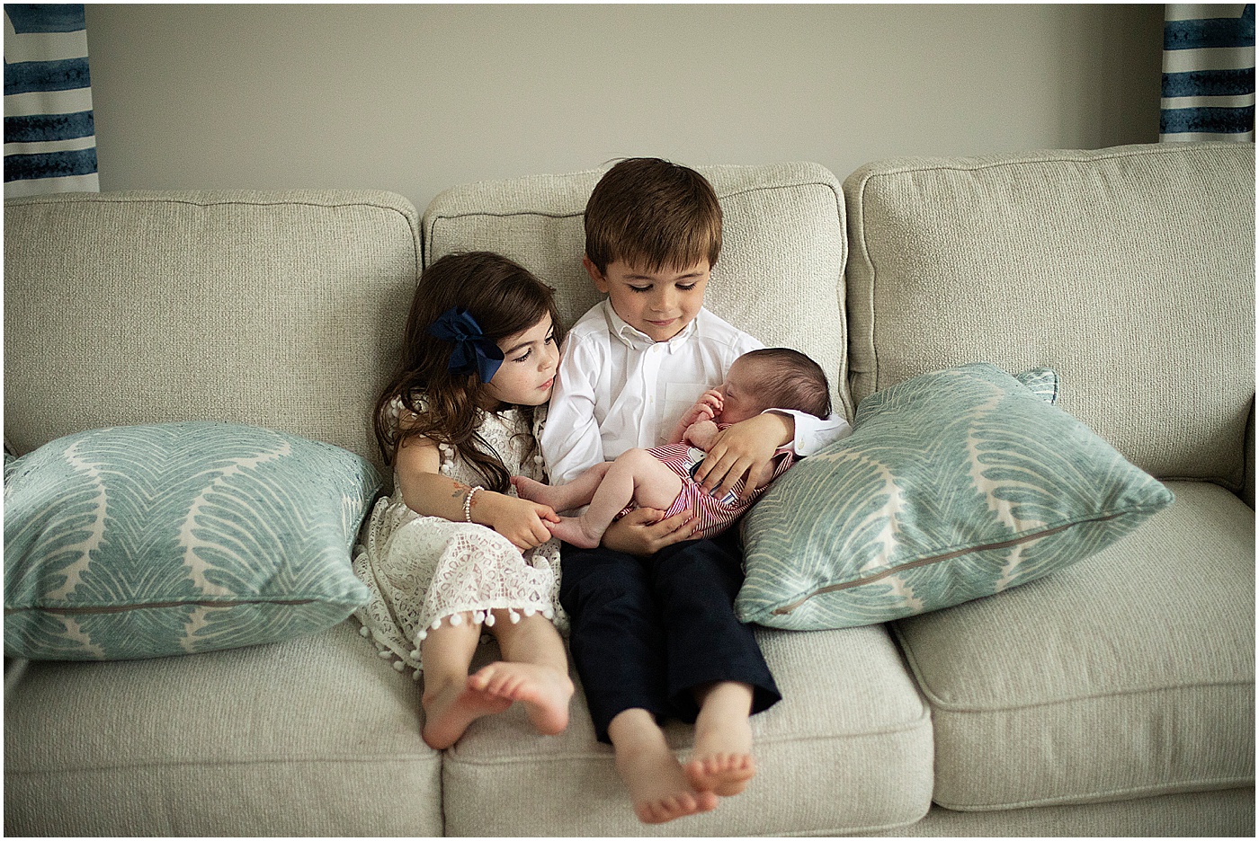 big brother and big sister cuddling newborn sibling on couch