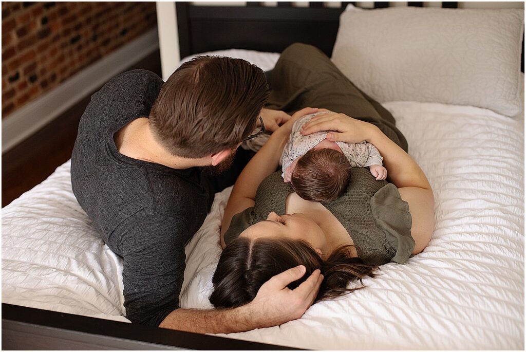 baltimore mom, dad, and newborn cuddled on bed during in home newborn photography session