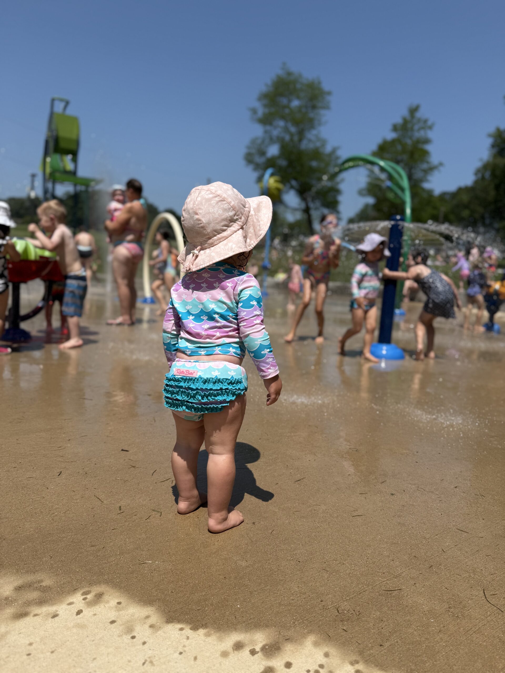 young child standing at the edge of baltimore splash pad